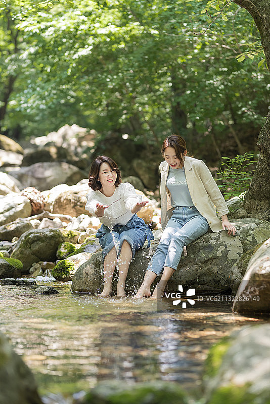 母女坐在森林水边的岩石上图片素材
