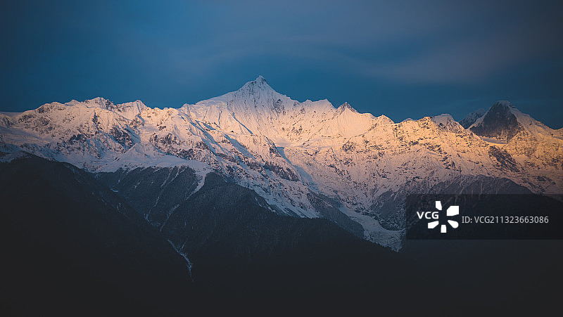 清晨的卡瓦格博峰，一轮余晖洒落在半山腰上，被白雪映射的金黄图片素材