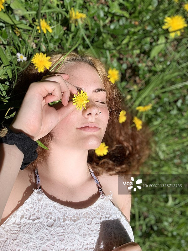 闭着眼睛躺在田野里手持鲜花的女青年图片素材