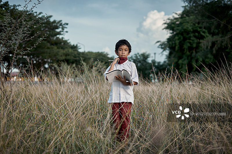 印度尼西亚，班达亚齐：男孩在田野里拿着书图片素材
