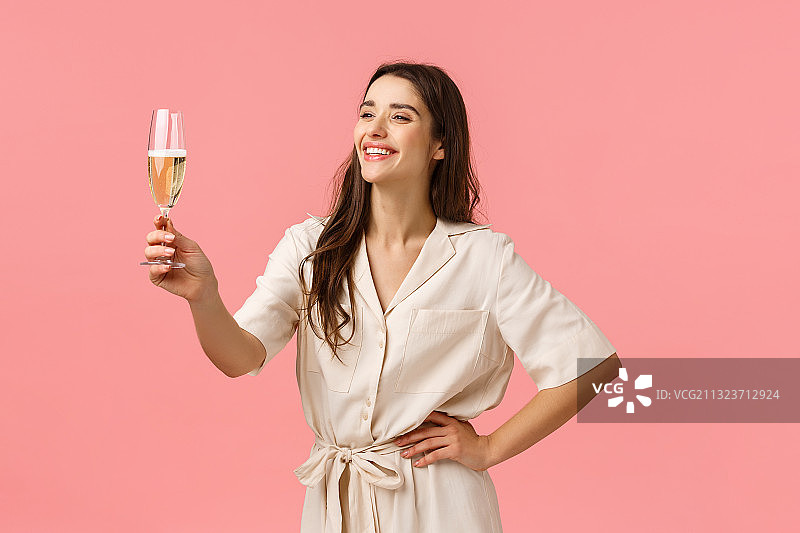 微笑的年轻女人拿着香槟杯站在粉色背景前。图片素材