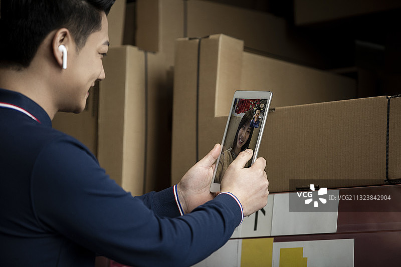 青年男子使用平板电脑在物流仓库帮助顾客展示产品图片素材