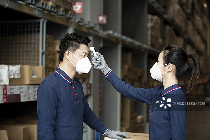两个青年男女戴着口罩和手套测体温在物流仓库工作肖像图片素材