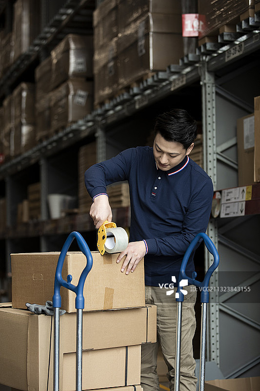 青年男子在物流仓库打包封箱工作肖像图片素材