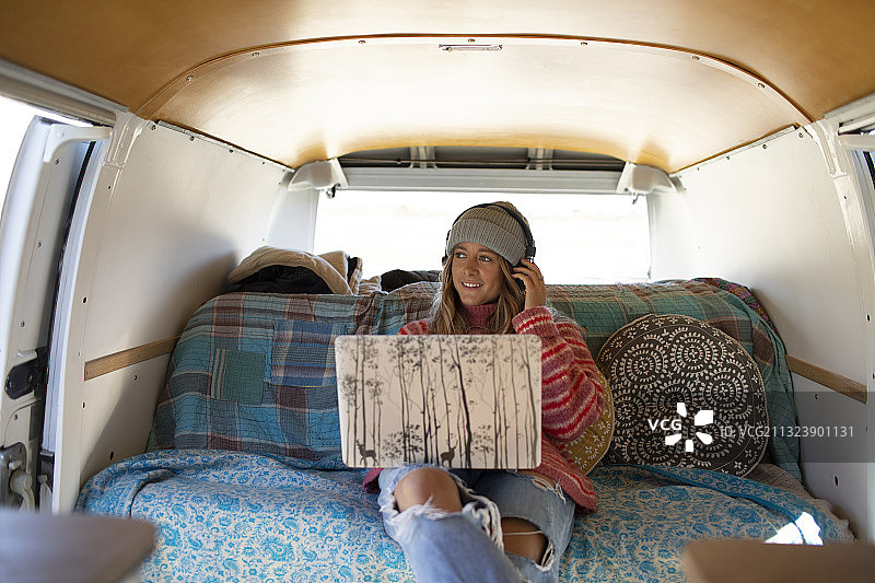年轻女子戴着耳机，在露营车里使用笔记本电脑图片素材