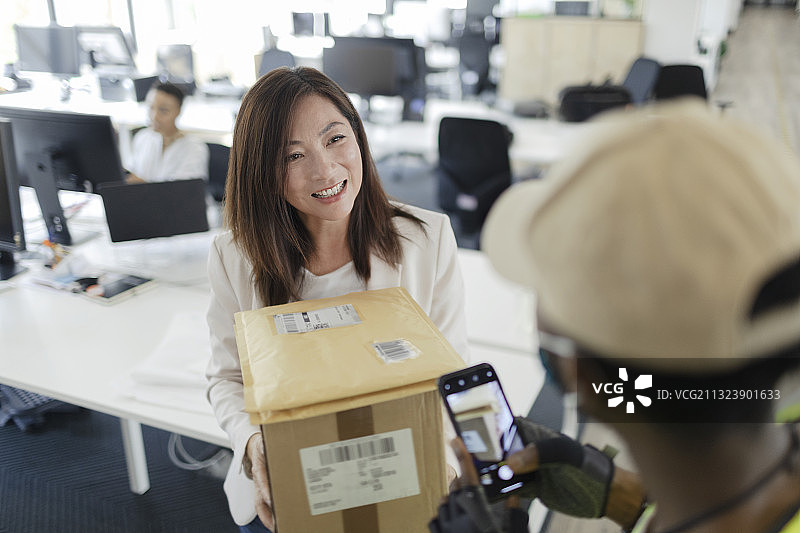 快乐的女商人从办公室的快递员那里收到包裹图片素材