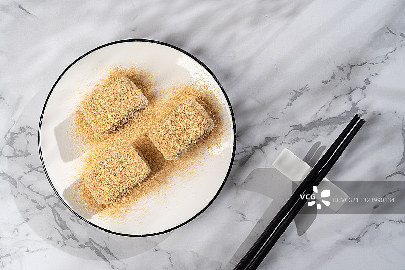 浅色纯色背景上盘子里的北京传统特色糕点小吃驴打滚图片素材