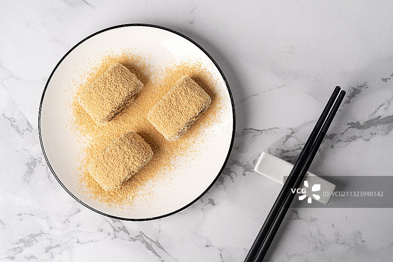 浅色纯色背景上盘子里的北京传统特色糕点小吃驴打滚图片素材