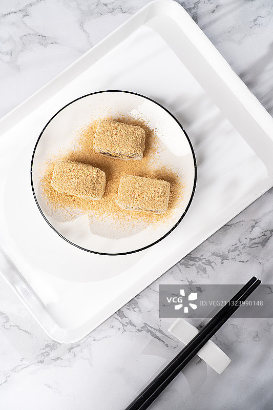 浅色纯色背景上盘子里的北京传统特色糕点小吃驴打滚图片素材