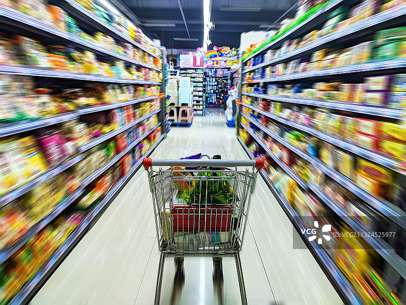 超市购物车在放满商品的动态模糊效果的货架中间图片素材