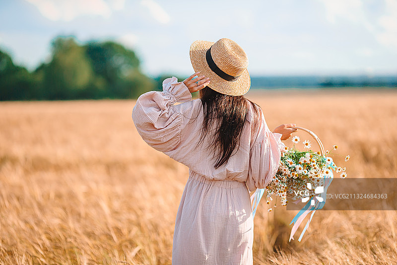 女人站在田野上手捧鲜花的背影图片素材