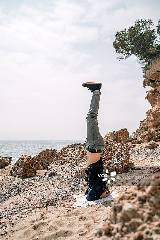 女人在西班牙海滩岩石上倒立图片素材