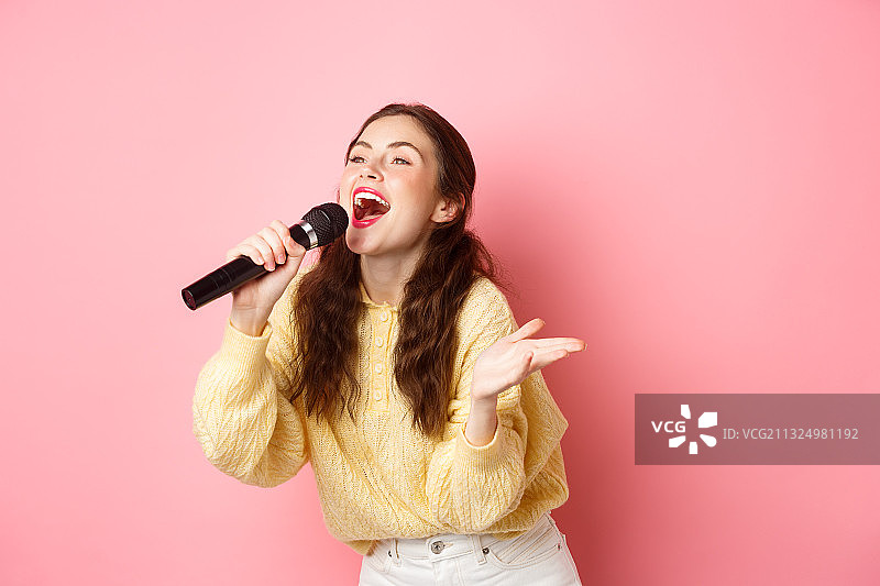 年轻女子在粉色背景前对着麦克风唱歌图片素材