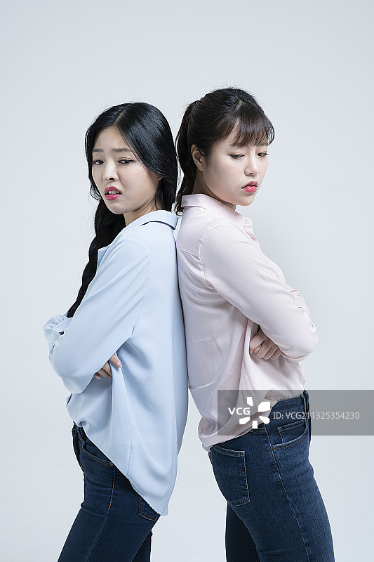 生气的亚洲姐妹背靠背站立图片素材