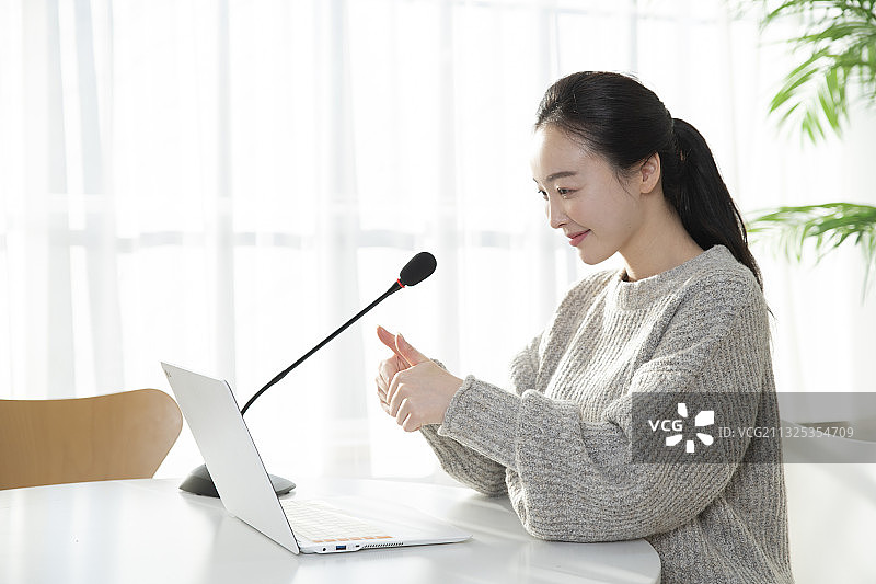 亚洲女人用笔记本电脑在麦克风上讲话，远程在线课堂教学，视频会议概念图片素材