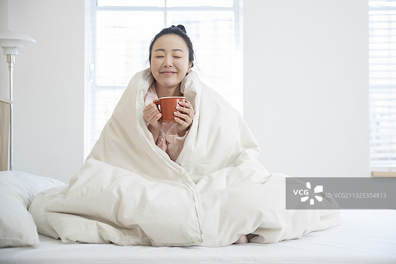 在毯子下喝热茶、咖啡的睡衣亚洲女人图片素材