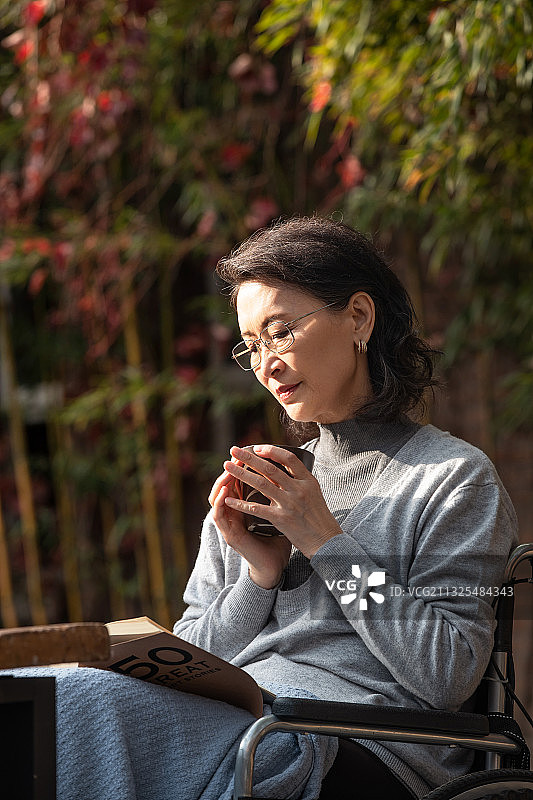 户外老年女人坐在轮椅上看书图片素材