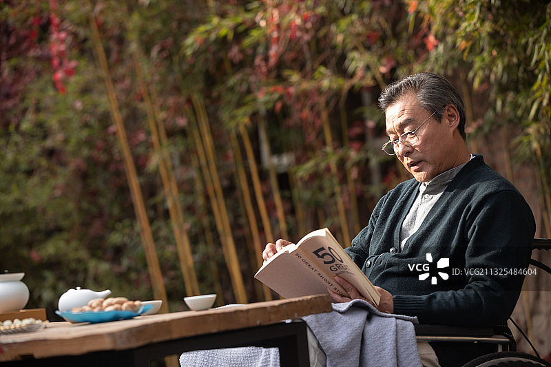 户外老年男人坐在轮椅上看书图片素材