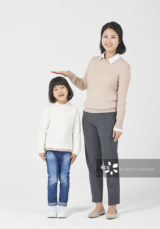 妈妈在白色背景前测量女儿身高图片素材