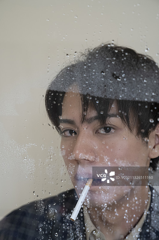 男人在雨中窗边抽烟的肖像图片素材