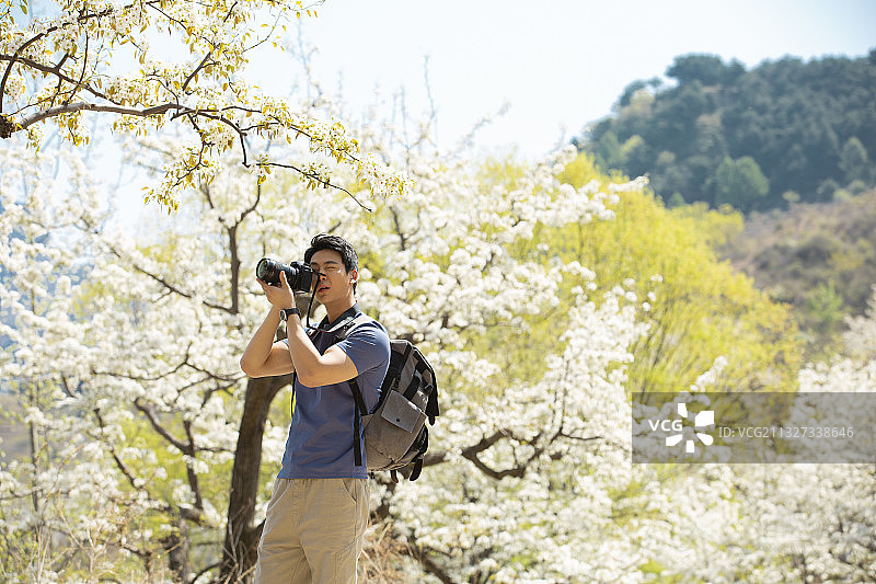青年男子户外旅行拿着单反相机拍照图片素材
