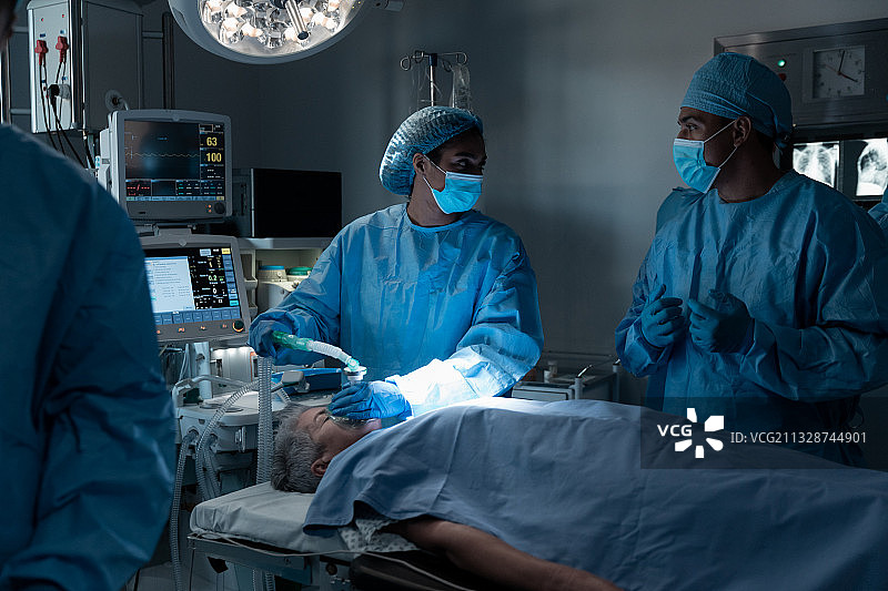 不同行业的外科医生戴着口罩和防护服在手术中镇静病人图片素材