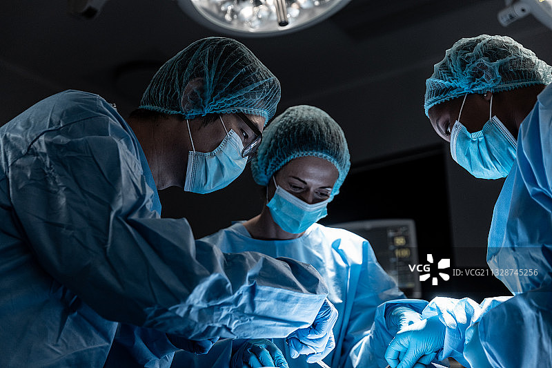 一群不同肤色的男女外科医生在手术室里戴着口罩做手术图片素材