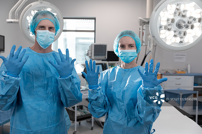 戴着口罩站在手术室里的白人男女外科医生肖像图片素材