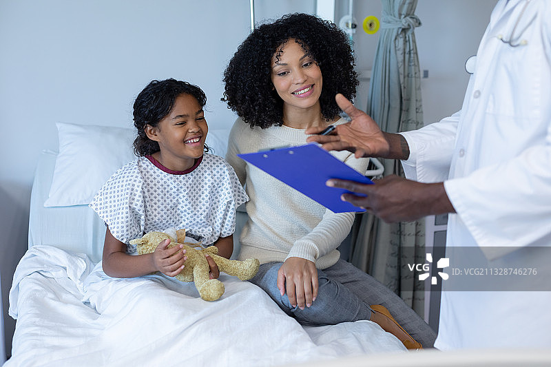 微笑的混血母亲和生病的女儿在医院病床上，听医生讲话图片素材