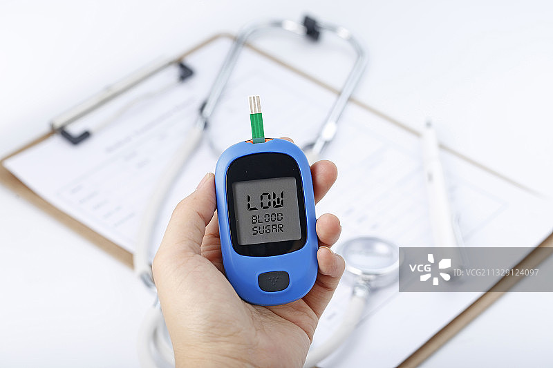 手拿着血糖仪测量血糖在听诊器和病历夹背景前图片素材
