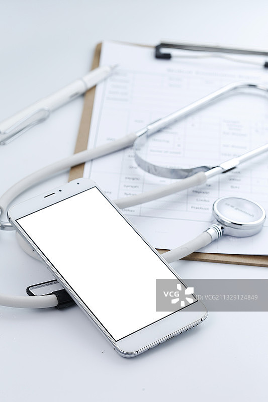 手机听诊器和病历夹放在白色桌面上图片素材