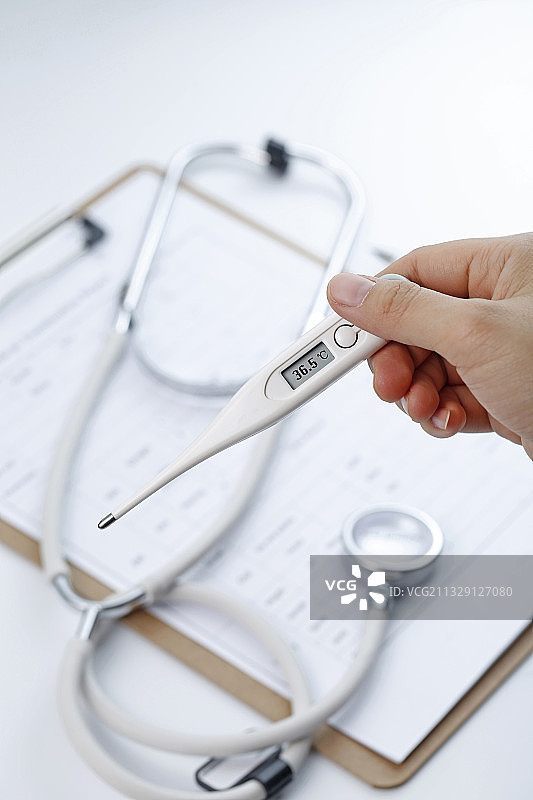 手拿着电子体温计在病历夹和听诊器背景前图片素材