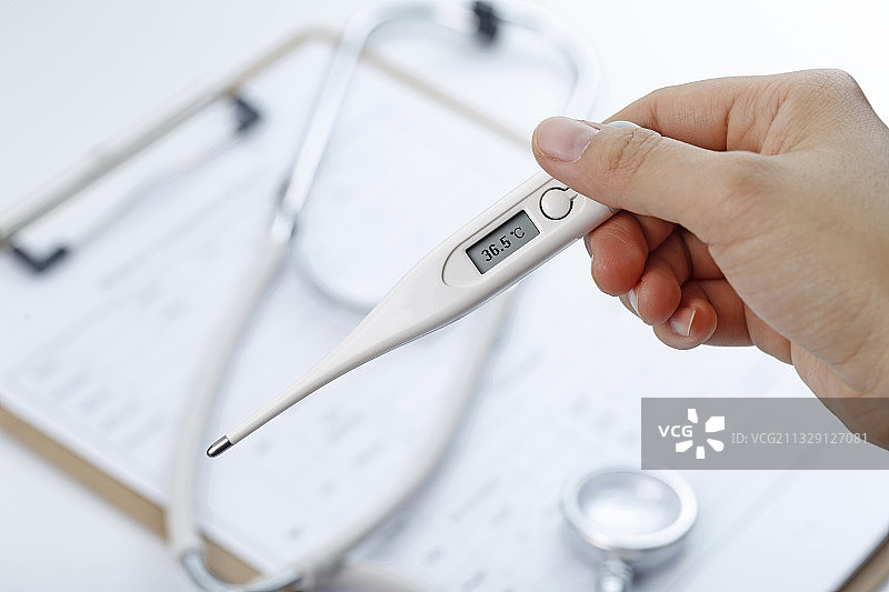 手拿着电子体温计在病历夹和听诊器背景前图片素材