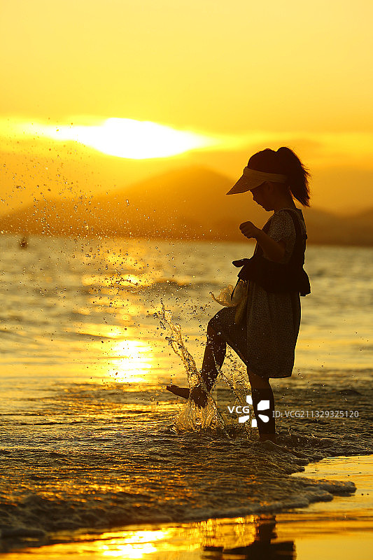 初夏，一小朋友在海南省三亚湾夕阳中戏水玩耍。图片素材