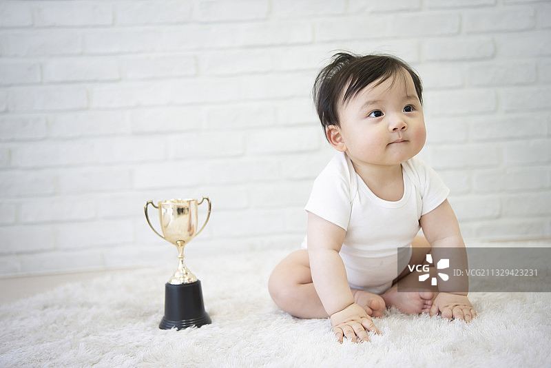 可爱的宝宝坐在奖杯旁的垫子上图片素材