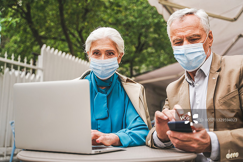 年长夫妇戴着口罩在户外用笔记本电脑和手机约会图片素材