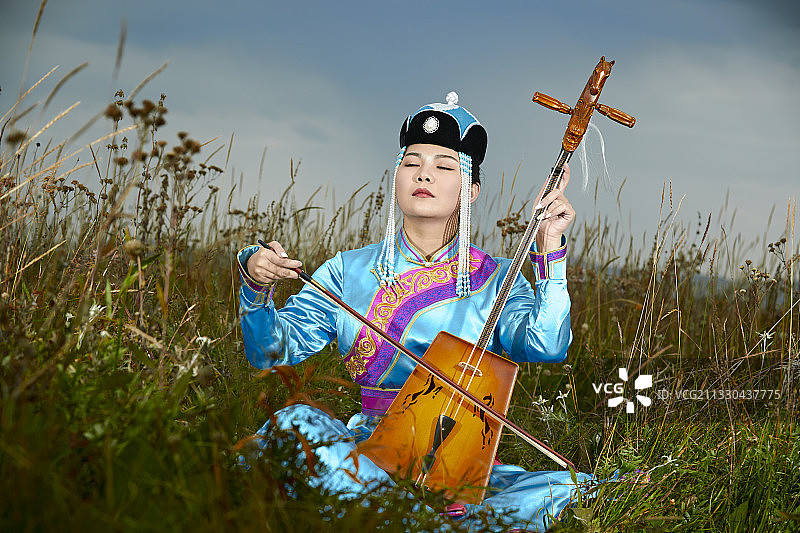 草原上身穿蒙古族服饰演奏马头琴的少女图片素材