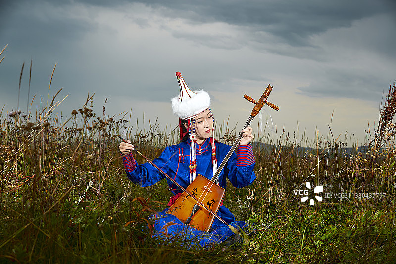 草原上身穿蒙古族服饰演奏马头琴的少女图片素材