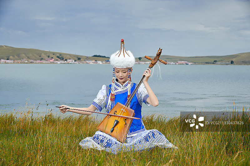 草原上身穿蒙古族服饰演奏马头琴的少女图片素材