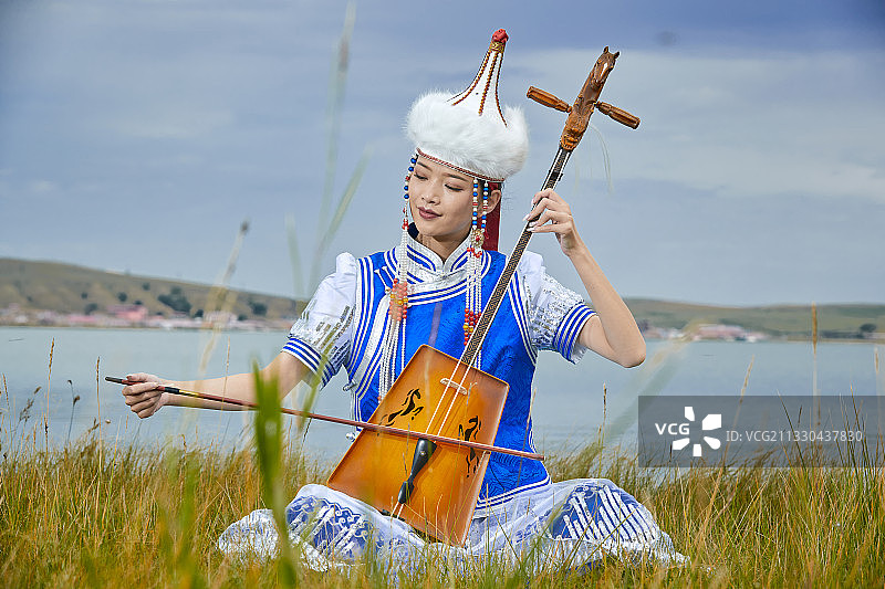 草原上身穿蒙古族服饰演奏马头琴的少女图片素材