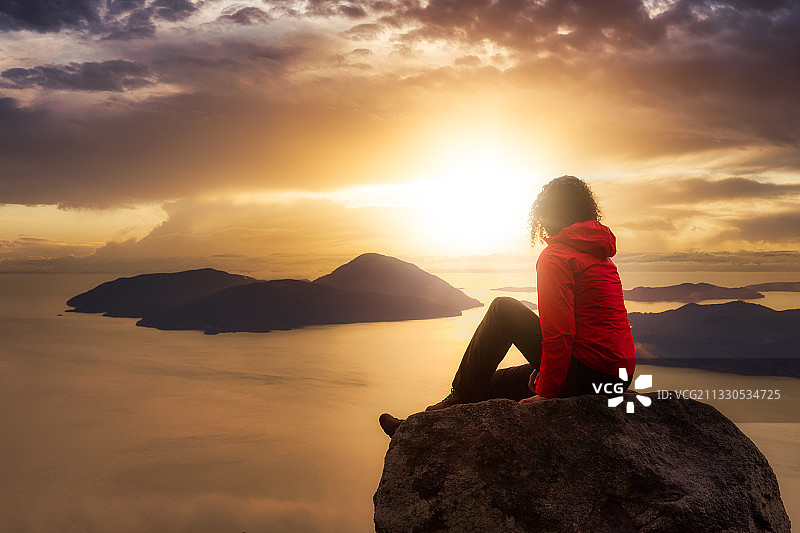 日落时分，坐在岩石上欣赏天空的女人图片素材