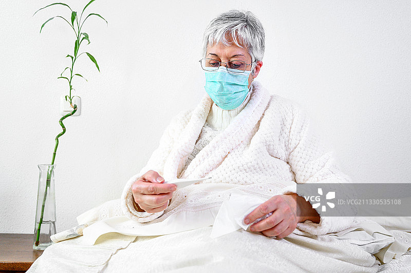 新冠肺炎期间，戴着防护口罩的生病老年妇女卧床不起图片素材