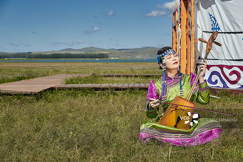 草原上穿着蒙古族传统服饰演奏马头琴的少女图片素材
