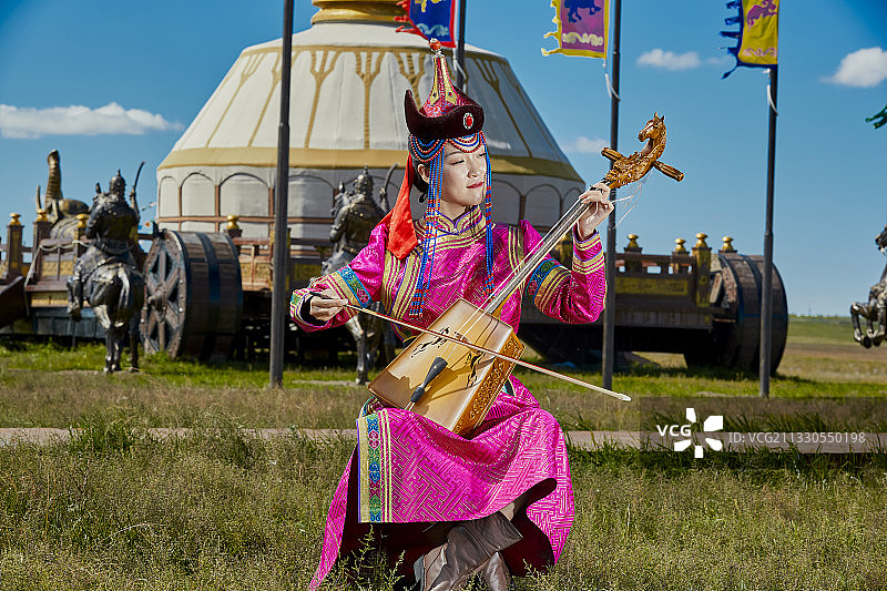 草原上穿着蒙古族传统服饰演奏马头琴的少女图片素材