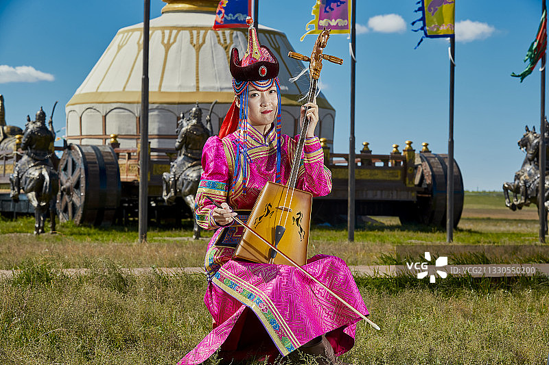 草原上穿着蒙古族传统服饰演奏马头琴的少女图片素材