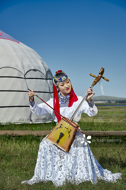 草原上蒙古包前穿着蒙古族传统服饰演奏马头琴的少女图片素材