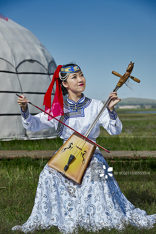 草原上蒙古包前穿着蒙古族传统服饰演奏马头琴的少女图片素材