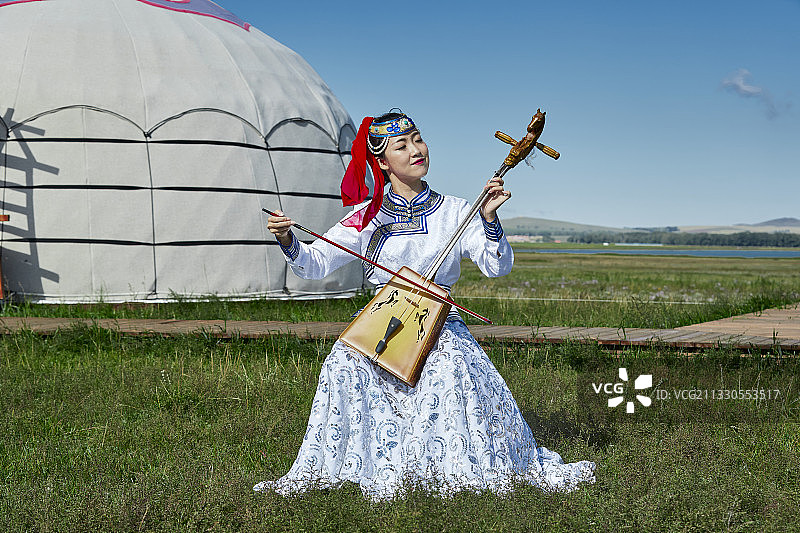 草原上蒙古包前穿着蒙古族传统服饰演奏马头琴的少女图片素材