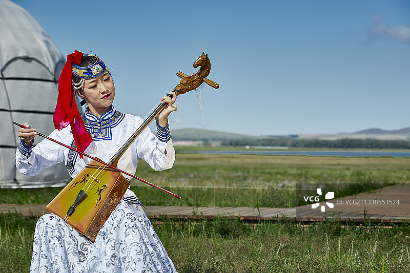 草原上蒙古包前穿着蒙古族传统服饰演奏马头琴的少女图片素材