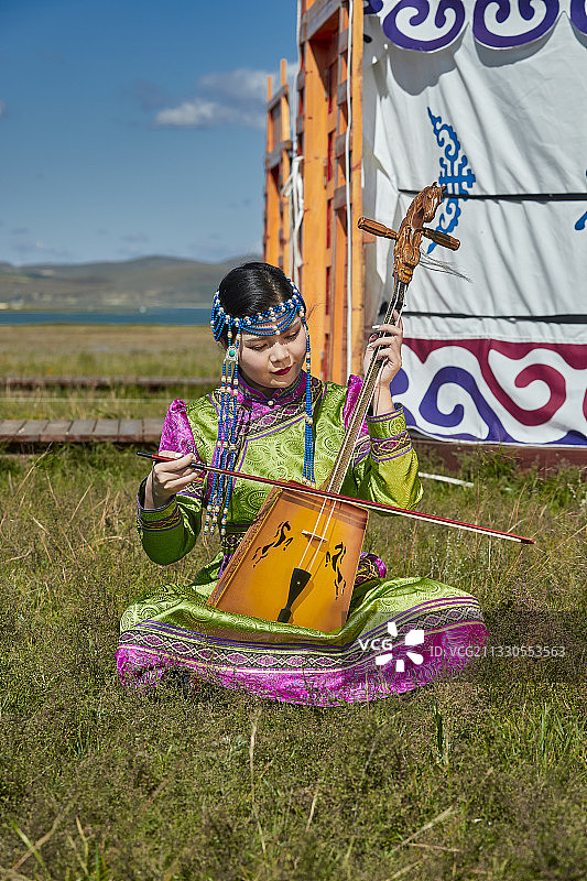 草原上穿着蒙古族传统服饰演奏马头琴的少女图片素材
